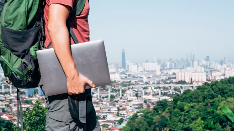 Traveler with a laptop overlooking a city from a hillside